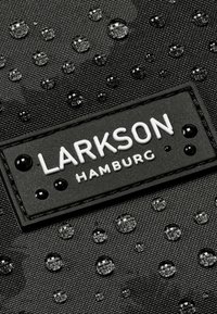 Čierna textúrovaná látka obsahuje vodné kvapky a štvorec s logom "LARKSON HAMBURG" v bielej farbe, obklopený čiernymi akcentmi.