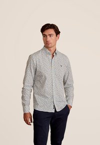 Overhemd met knoopsluiting op een witte basis, voorzien van een kleurrijk bloemenpatroon. Gemaakt van stof met een gladde textuur en een klassiek kraagontwerp.