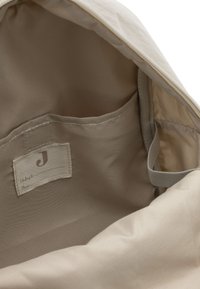 Lichtbeige stoffen interieur van een tas met een gestikt label en een klein vak, met een gladde textuur en minimale zichtbare hardware.