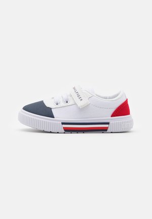 Sneaker in tela bianca con punta in navy, dettaglio rosso sul tallone e suola a righe rosse, bianche e blu. Strap in velcro e dettagli con lacci.