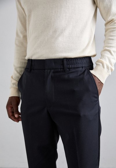 Pantaloni negri cu o croială lejeră, talie elastică și buzunare laterale, asortați cu un pulover tricotat de culoare bej deschis. Textură de țesătură moale.