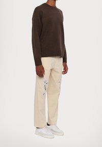 Brown knitted sweater with ribbed cuffs, paired with cream-colored pants featuring silver floral embroidery and white sneakers.
