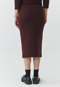 Gonna midi in magenta a maglia con una forma aderente, caratterizzata da uno spacco laterale. Indossata con scarpe chunky nere e calze nere a lunghezza caviglia.