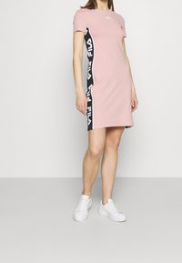 Różowa sukienka z krótkim rękawem, z czarnym bocznym panelem z powtarzającym się białym napisem. Wykonana z miękkiego materiału. Połączona z białymi trampkami.