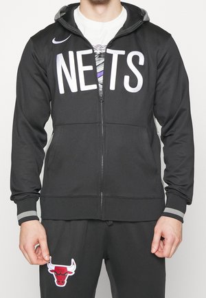 Černá zipová bunda s velkým bílým nápisem "NETS". Ozdobena šedými manžetami a kapucí, v kombinaci se šedými sportovními kalhotami s červeným logem býka.