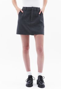 Grijze wolmix mini-jurk met een aansluitende taille, subtiele voorplooien en zijzakken, gecombineerd met zwarte veterschoenen en witte sokken.