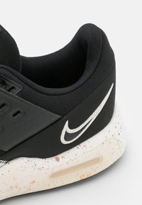 Sneaker nera con superiore testurizzato, caratterizzata da un logo Swoosh bianco prominente e una suola intermedia beige maculata con imbottitura d'aria visibile.