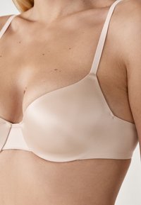 Reggiseno push-up nudo con texture satinate lisce, coppe sagomate e spalline regolabili. Design senza cuciture che migliora il comfort e il supporto.