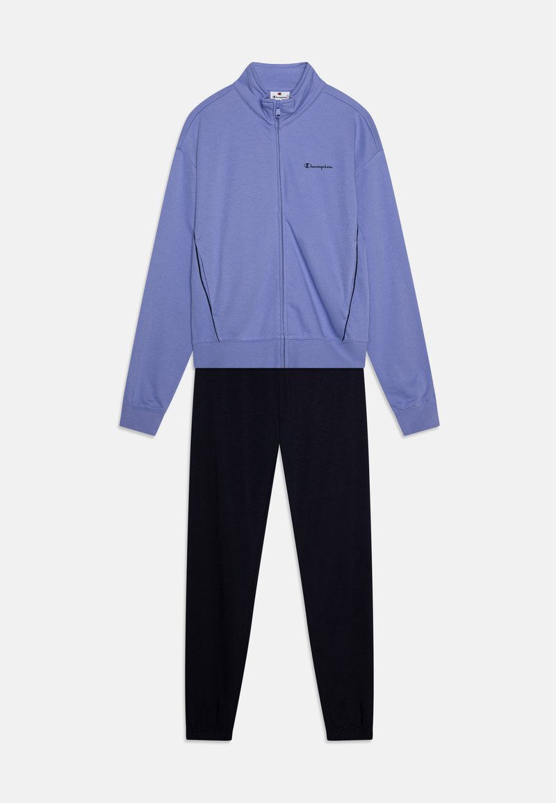 Giacca a zip viola con colletto alto, logo nero e due tasche laterali, abbinata a pantaloni tuta neri a gamba stretta. Materiale morbido, design casual.