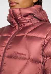 Primer plano de una persona que lleva una chaqueta puffy rosa de Berghaus con un alto cuello, mostrando el logo de la marca en el pecho.