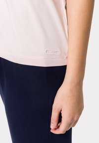 Camisa de manga corta rosa claro con una textura suave, que presenta un logotipo sutil en el dobladillo, combinada con leggings oscuros azul marino.