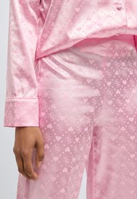 Rosa Satinh-Pyjama-Set mit einem Muster aus Herzen und Punkten, mit Kragen, Knopfleiste und weicher Textur.