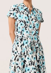 Šaty s krátkým rukávem s modro-černým květinovým potiskem na bílém pozadí, s límečkem a zavazováním v pase.