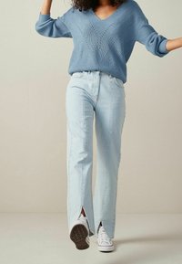 Pull tricoté bleu clair avec col en V ; associé à un jean délavé clair avec des fentes à l'ourlet et des baskets blanches.