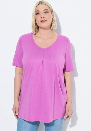 Top rosa chiaro a maniche corte con scollatura tonda e pieghe sottili sul petto, realizzato in tessuto morbido. Indossato con jeans azzurri chiari.