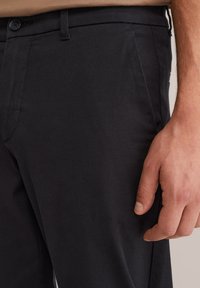 Pantaloni neri in cotone misto con una texture liscia, taglio slim e tasche laterali. Presentano una chiusura con bottone e passanti per cintura in vita.