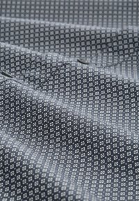 Marineblauwe stof met een wit geometrisch patroon van kleine diamanten en vierkanten, met een gladde textuur en een lichte glans.