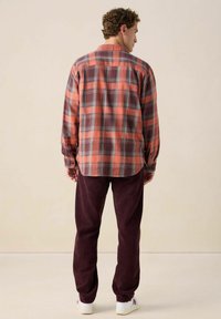 Rood en grijs geruite blouse met lange mouwen en een button-down kraag, gecombineerd met maroon corduroy broeken en witte sneakers.
