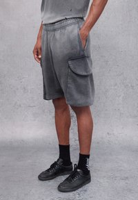 Shorts grigi con tessuto morbido, dotati di un cintura elastica, due tasche laterali e un branding discreto. Abbinati a sneakers e calzini neri.