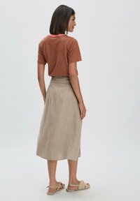 Gestreiftes kurzärmliges braunes und orangefarbenes Hemd kombiniert mit einem mittelgroßen beigen Leinenrock und beigen flachen Sandalen. Ein weicher Stoff mit lässigem Schnitt.