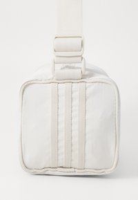 Bolsa de tela blanca de forma rectangular, con una superficie texturizada, una correa gruesa y cierre de hebilla simple. Detalles de costura reforzada.