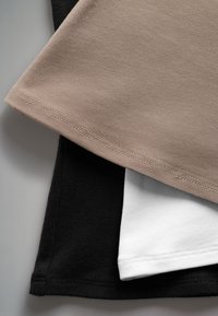 Drie katoenen T-shirts in zwart, beige en wit. Close-up toont de stoftextuur en zoom met stikdetails.
