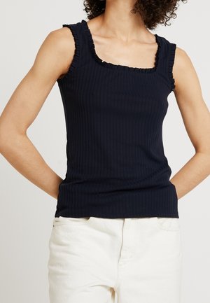 Granatowy prążkowany top bez rękawów z kwadratowym dekoltem i falbaniastymi akcentami na ramionach, w zestawieniu z jasnymi spodniami. Widoczny detal faktury tkaniny.