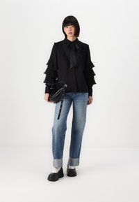 Blusa nera con maniche a sbuffo, collarino e dettaglio con fiocco, abbinata a jeans a gamba larga blu chiaro e scarpe nere chunky. Inclusa borsa nera.