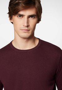 Bordowy sweter z okrągłym dekoltem o prążkowanej fakturze, charakteryzujący się dopasowanym krojem i minimalistycznym wykończeniem dekoltu, zaprezentowany na neutralnym tle.