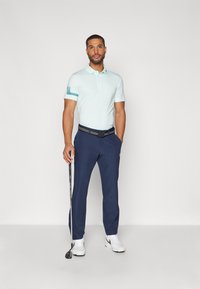 Helles blaues Poloshirt mit einem gemusterten Kragen und dunkelblauen Hosen. Weiße Sneaker und ein Golfclub in der rechten Hand. Einfaches Design.