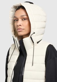 Puffer-Weste in Off-White mit einem gesteppelten Muster, verstellbare Kapuze, hohem Kragen und schwarzer Reißverschlussdetails auf der Vorderseite.