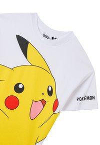T-shirt bianca in cotone con una grande grafica gialla di Pikachu sulla parte anteriore, con dettagli neri e la scritta 'POKÉMON' stampata sulla manica.