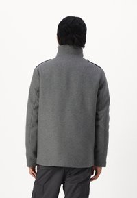 Abrigo de lana gris con un cuello alto, diseño sencillo y construcción sin costuras, llevado sobre pantalones cargo oscuros.