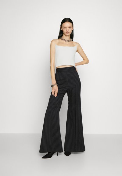 Fehér, textúrált crop top, fekete csíkos, bő szárú nadrág, magas derekú, fekete tűsarkú cipő, ezüst vagány nyaklánc kiegészítőként.