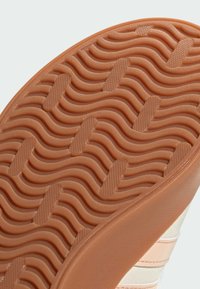 Gummisul för sneakers med ett vågigt mönster; färgen är ljusbrun med subtil textur och räfflor för bättre grepp.