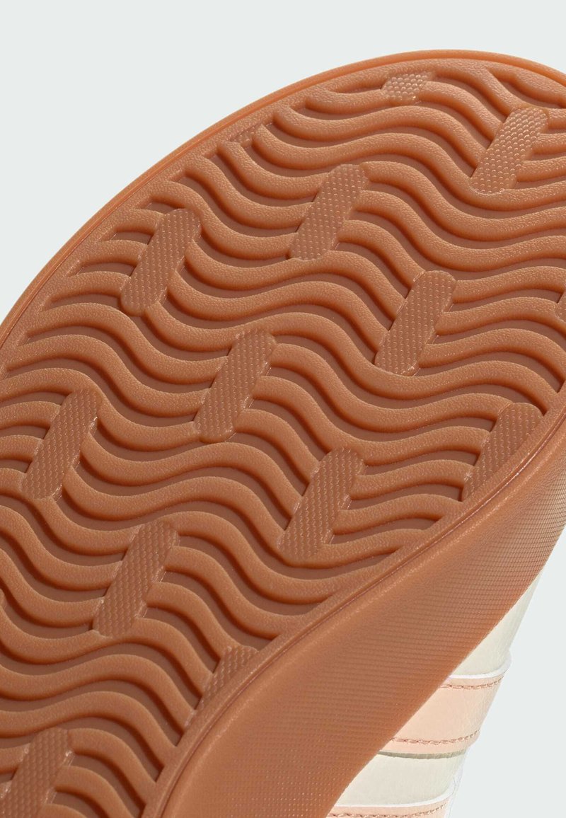 Semelle en caoutchouc de sneaker avec un motif de crampons ondulé ; la couleur est brun clair avec une texture subtile et des crêtes pour une meilleure adhérence.