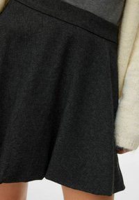 Czarna spódnica rozkloszowana z teksturowanej tkaniny, z dopasowanym paskiem w talii i warstwowym krojem, minimalnie zdobiona, w połączeniu z lekkim swetrem.