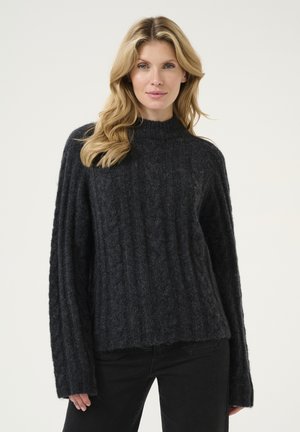 Mørkegrå strikket trøje med høj hals, ribbet struktur og brede, lange ærmer. Kanten er let cropped. Parret med sorte jeans.