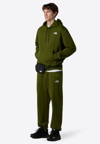 Groene hoodie en bijpassende joggers gemaakt van een katoenmix, met een voorzak en logo-accenten. Zwarte heuptas en schoenen.