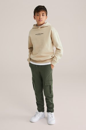 Beige hoodie med teksten "BLUE RIDGE DENIM", parret med olivengrønne cargo-bukser med lommer og hvide sneakers. Enkelt, afslappet outfit.
