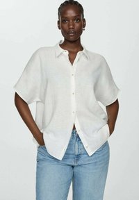White linen shirt with a collar, short sleeves, and a button-up front. Paired with light blue denim jeans. Smooth, breathable texture.