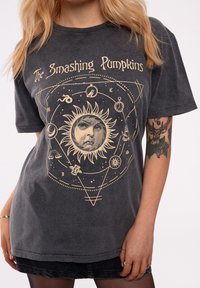 Gray cotton t-shirt featuring gold graphic design of a sun with a face, celestial symbols, and text "The Smashing Pumpkins." Short sleeves.