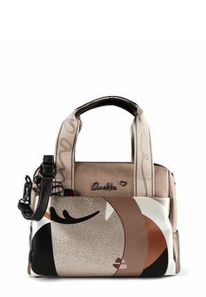 Beige und braune Handtasche mit beige gemusterten Griffen, schwarzem verstellbarem Riemen und abstraktem Gesichtsmotiv mit kleinen Nieten-Details auf der Fronttasche.