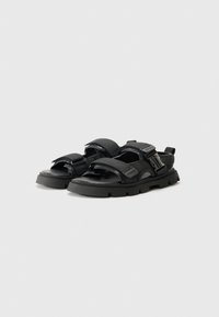 Black sandals with a chunky sole, open toe, and adjustable straps made of textured fabric and smooth synthetic material.
