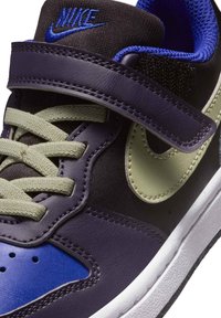 Buty sportowe Nike z czarnymi, fioletowymi i niebieskimi skórzanymi panelami, zielonym logo w kształcie łyżwy, teksturowanymi akcentami z tkaniny oraz paskiem na rzep.