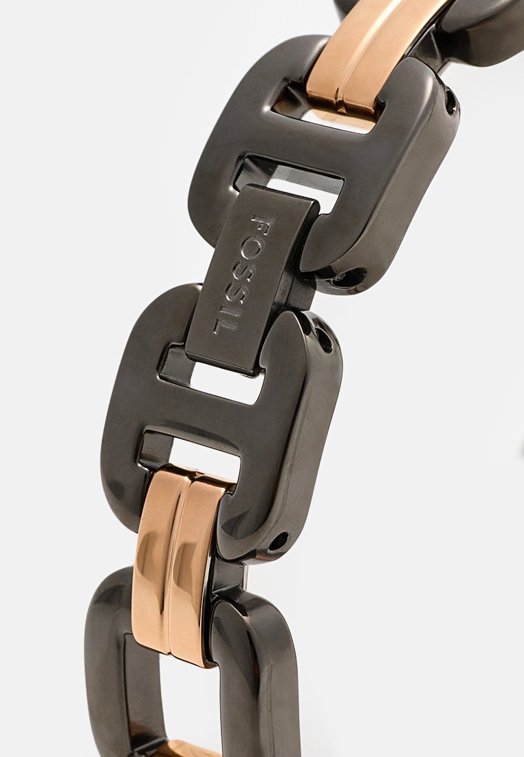 Bracelet à maillons noir et or rose avec des maillons métalliques rectangulaires, présentant des surfaces polies et un logo "FOSSIL" visible.