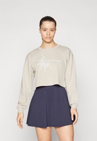 Beige kort hoodie med långa ärmar har en solgrafik och texten "State of mind"; parat med en marinblå utsvängd kjol.