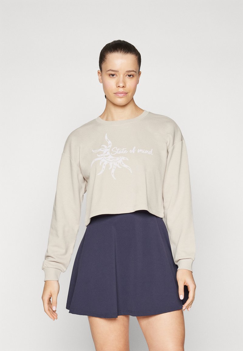 Beige kort hoodie med långa ärmar har en solgrafik och texten "State of mind"; parat med en marinblå utsvängd kjol.