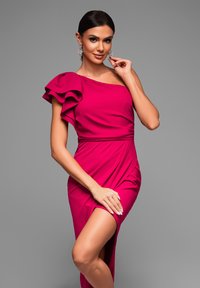 Robe fuchsia asymétrique à une épaule avec manche froncée, design drapé, fente haute sur la cuisse et texture lisse. Paire de boucles d'oreilles remarquables visibles.