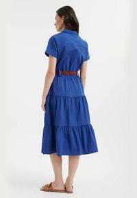 Abito di cotone blu con maniche corte, vita con cintura e orlo a ruches a strati. Presenta un colletto e una texture liscia.
